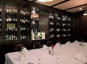 A restaurant with a long table set for dining, wine bottles on shelves, and a chandelier. - Sentinel Hotel (Portland)