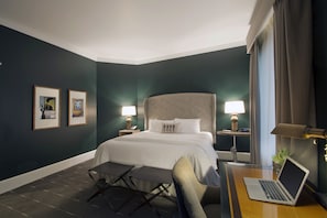 A hotel room with a large bed, bedside tables with lamps, a desk with a laptop, and framed pictures on the wall.