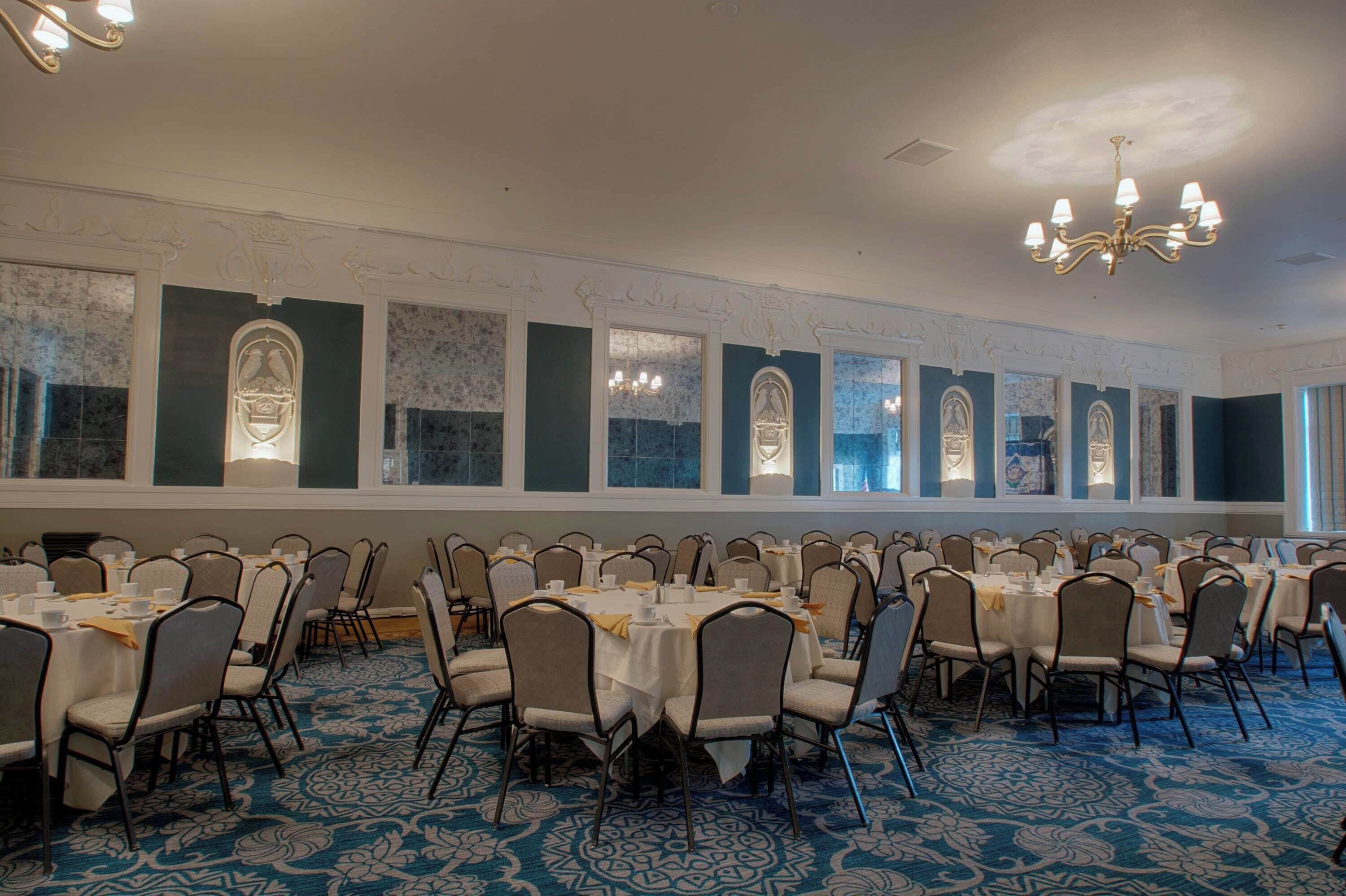 A banquet hall with multiple round tables, chairs, and a patterned carpet.