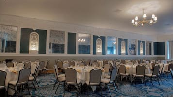 A banquet hall with multiple round tables, chairs, and a patterned carpet.
