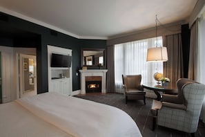 A hotel room with a bed, a television, a fireplace, a desk with a lamp, and a chair. - Sentinel Hotel (Portland)