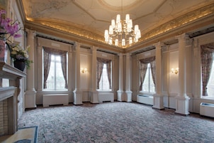 Una sala imponente con columnas ornamentales, un candelabro y amplias ventanas con cortinas.