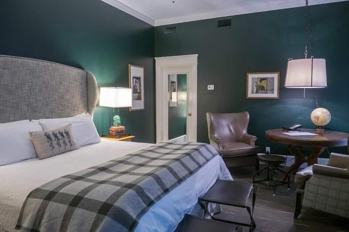 Una habitación de hotel con una cama grande, una silla, una mesita y una lámpara.