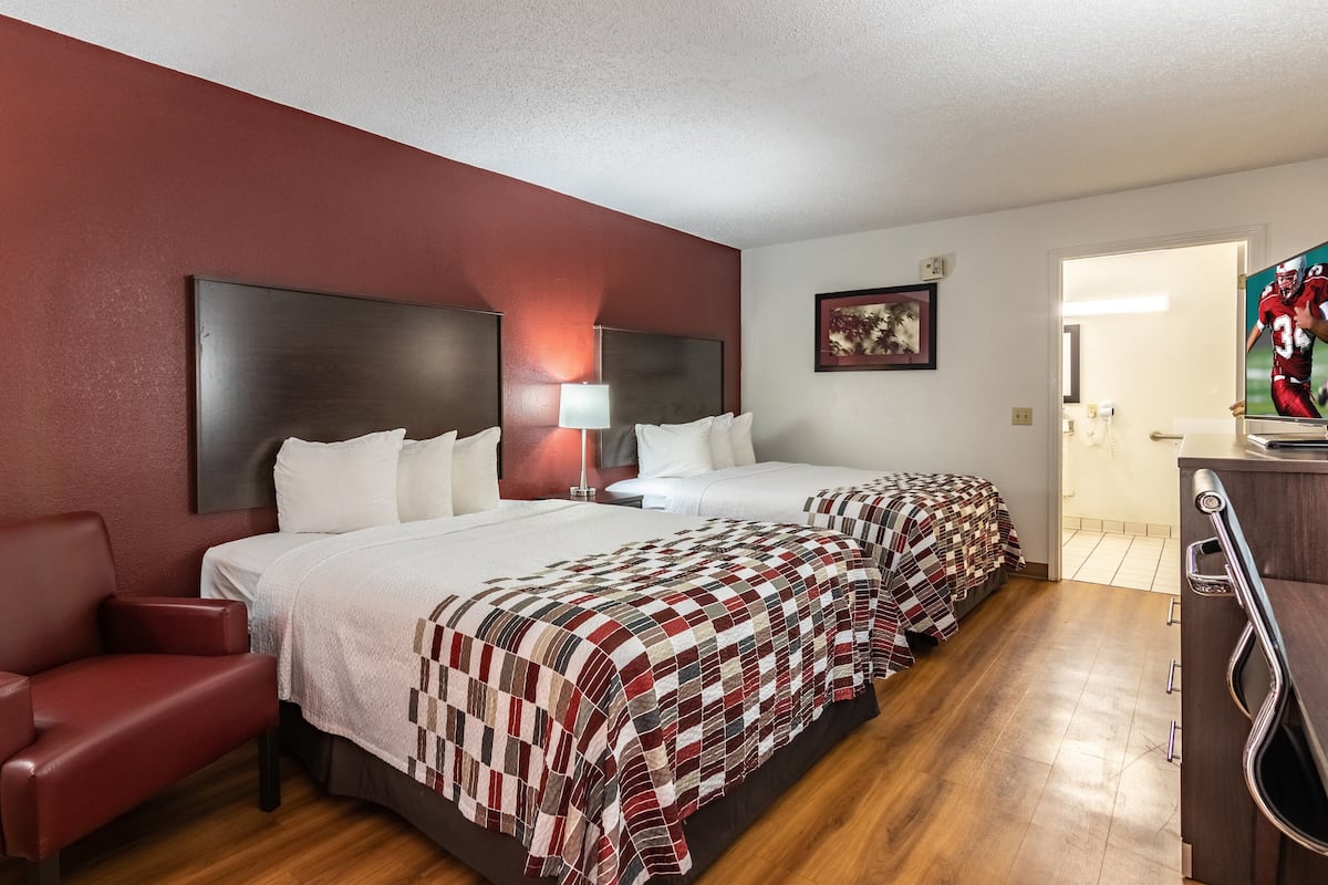 Una habitación de hotel con dos camas, un sillón rojo, un escritorio y un televisor.