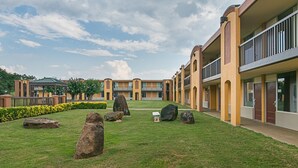 A courtyard with a lawn, large rocks, and a building with multiple balconies. - Red Roof Inn Forsyth (Forsyth)