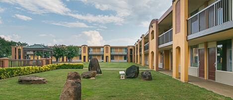 Un patio con césped, rocas grandes y un edificio con varios balcones.