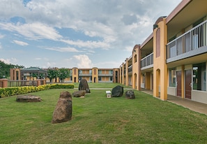 A courtyard with a lawn, large rocks, and a building with multiple balconies. - Red Roof Inn Forsyth (Forsyth)