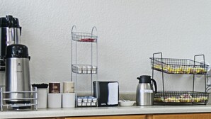 A kitchen counter with a coffee maker, sugar and cream containers, a thermos, a notebook, and a fruit basket. - Red Roof Inn Forsyth (Forsyth)