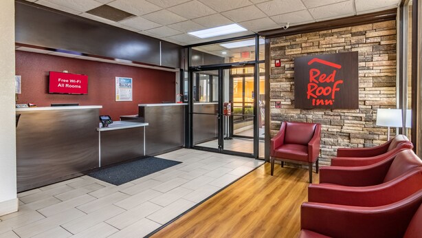 A Red Roof Inn reception area with a digital display, a reception desk, and a seating area with red chairs. - Red Roof Inn Forsyth (Forsyth)