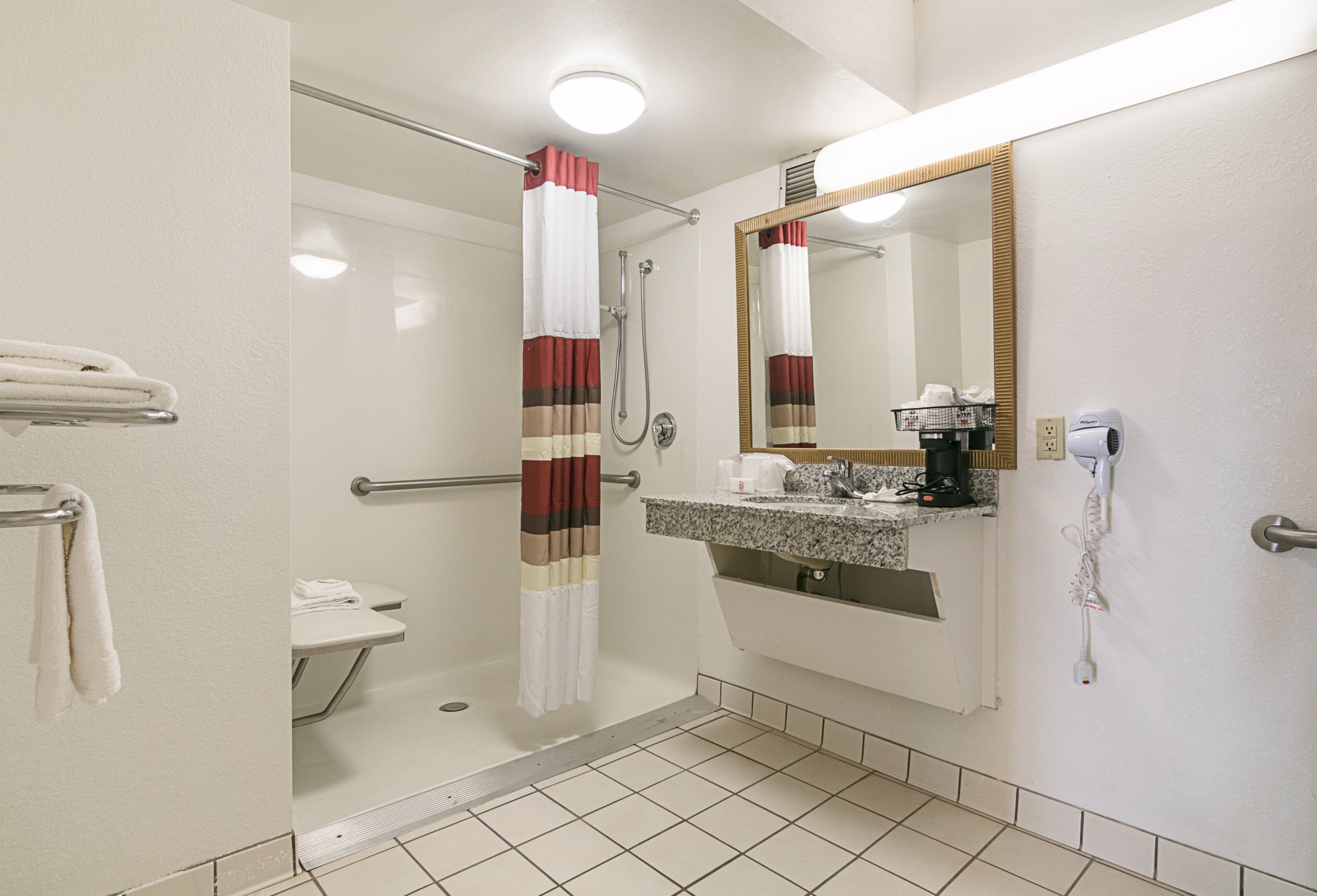 A hotel bathroom with a shower, a sink with a mirror, and a hairdryer on the wall.