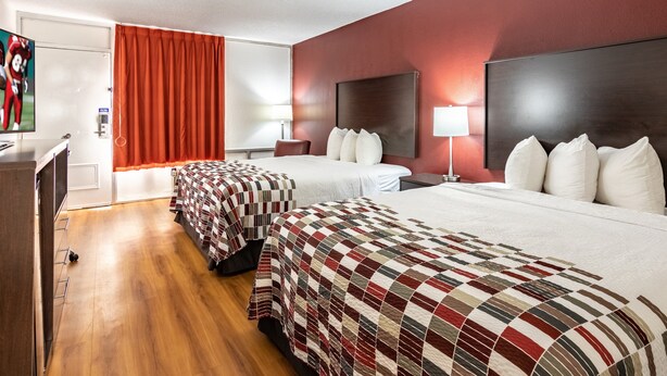 A hotel room with two beds, a desk, a TV, and a red curtain. - Red Roof Inn Forsyth (Forsyth)