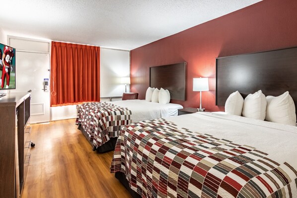 A hotel room with two beds, a desk, a TV, and a red curtain. - Red Roof Inn Forsyth (Forsyth)