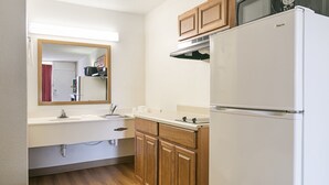 A compact kitchen with a white refrigerator, wooden cabinets, a microwave, and a sink with a mirror above it. - Red Roof Inn Forsyth (Forsyth)