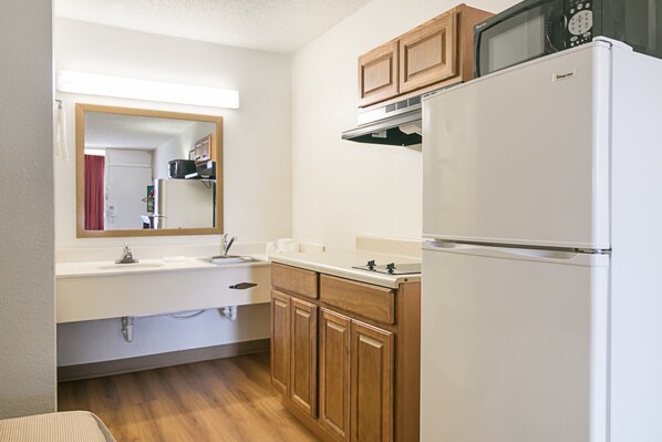 A compact kitchen with a white refrigerator, wooden cabinets, a microwave, and a sink with a mirror above it. - Red Roof Inn Forsyth (Forsyth)