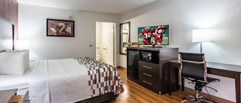 Habitación de hotel con cama, escritorio, silla, televisión y puerta que da a otra habitación.
