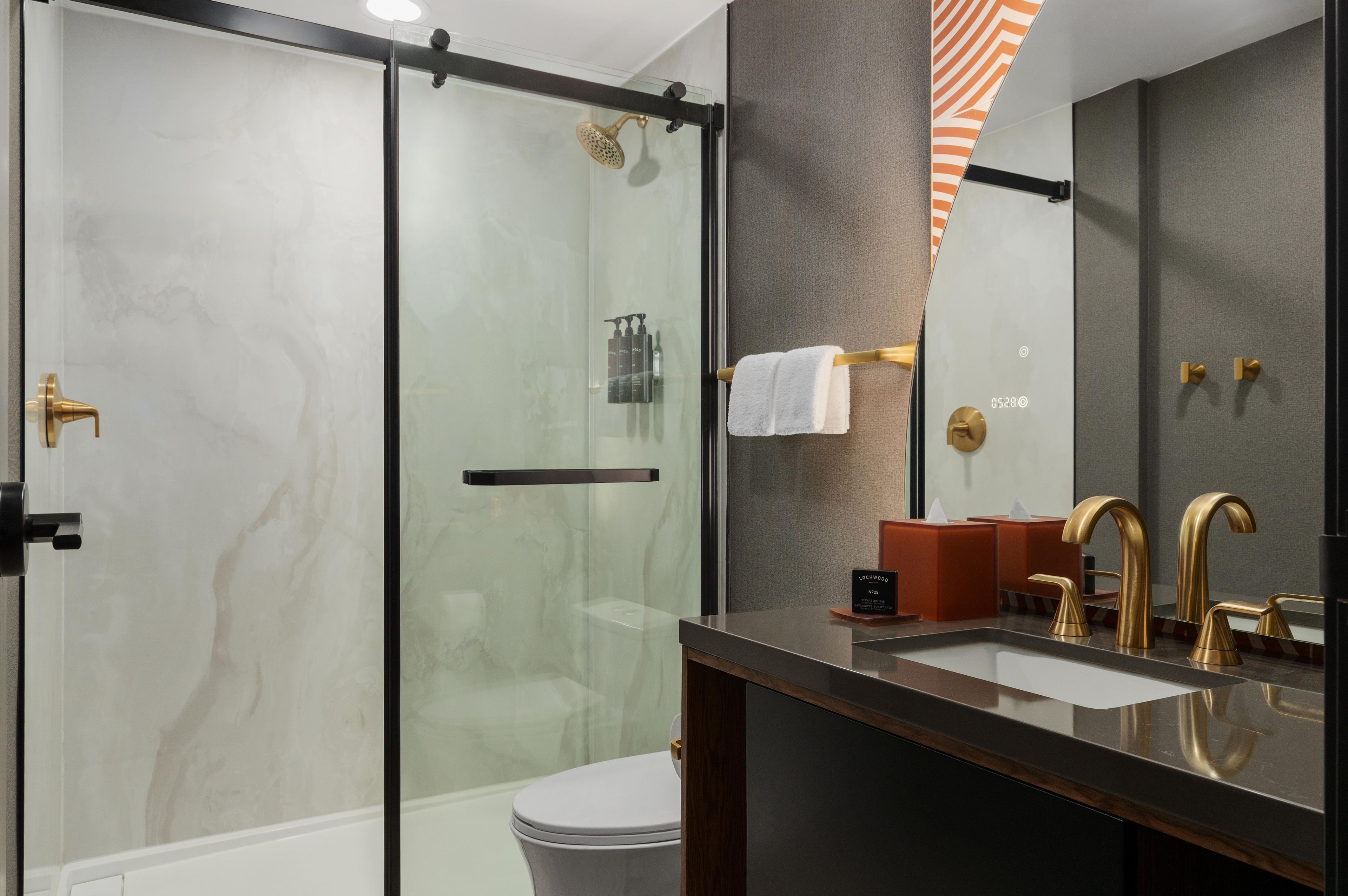 Une salle de bain moderne avec une douche à parois de verre, un meuble-lavabo doté d’un grand miroir et des toilettes.
