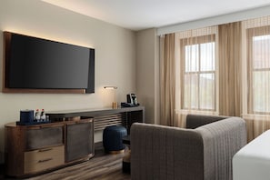 A hotel room with a flat-screen TV mounted on the wall, a desk with a lamp, a coffee maker, and a seating area with a sofa and armchairs. - The Berkeley Richmond, Outset Collection by Hilton (Richmond)
