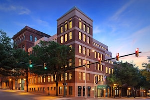 Un hotel de varios pisos con un diseño arquitectónico clásico y moderno, destacando un edificio en esquina con techo plano y una estructura adyacente más pequeña con fachada de ladrillo tradicional.