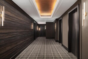 A modern hotel hallway with dark wood paneling, a checkered carpet, and a ceiling with recessed lighting. - The Berkeley Richmond, Outset Collection by Hilton (Richmond)