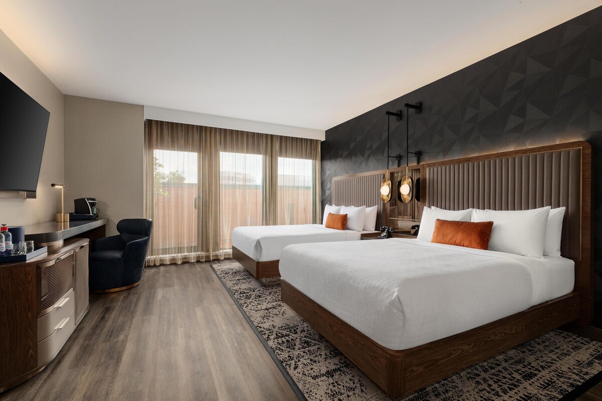 A hotel room with two beds, a desk, a chair, and a TV.