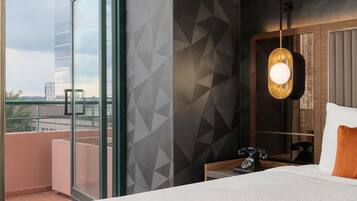 Ett hotellrum med ett stort fönster, en säng med ett vitt sänggavel, ett nattduksbord med en telefon och en vägg med ett geometriskt mönster.