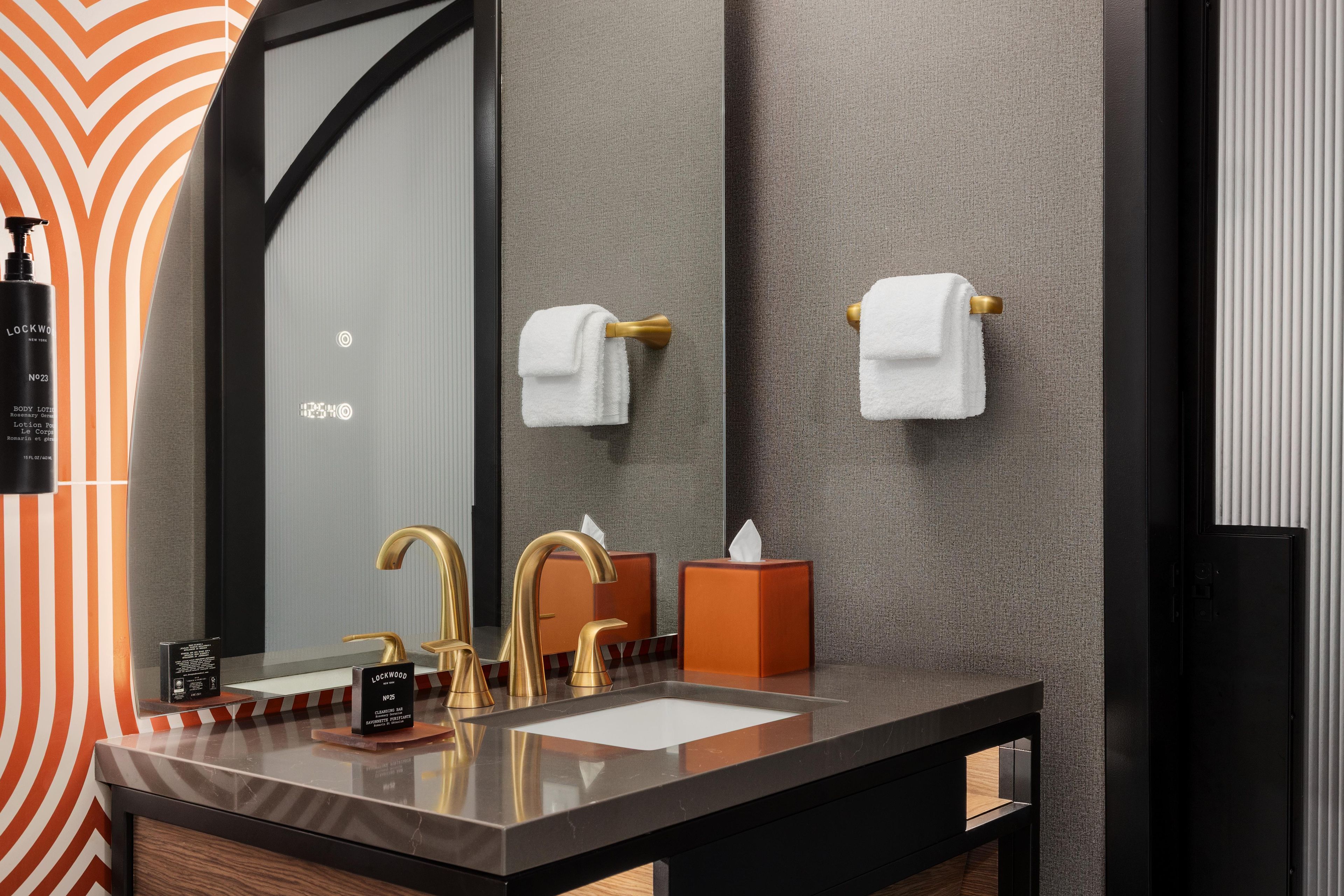 A bathroom with a modern design, featuring a large mirror, a black countertop, gold faucets, and a tissue box.