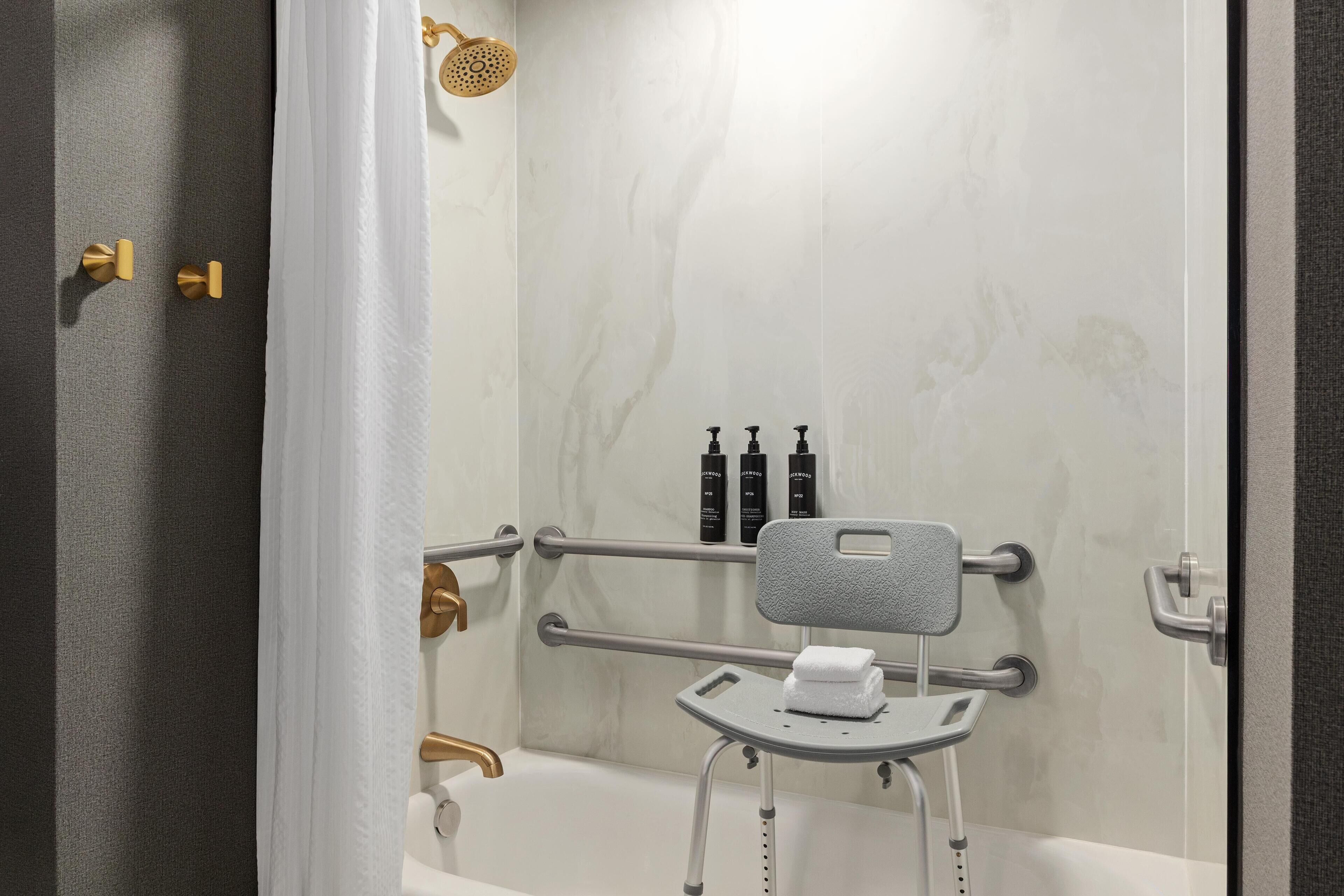 Une salle de bain équipée d’une douche, de barres d’appui, d’un porte-serviettes et d’un pommeau de douche à main.