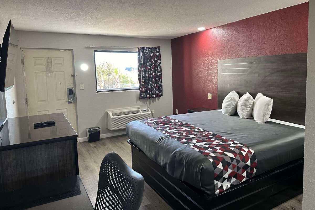 A hotel room with a bed, a desk, a chair, a window with curtains, and a radiator.