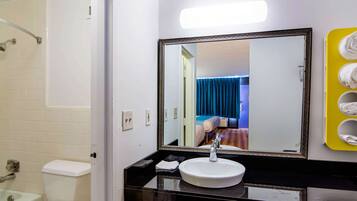 Un baño con lavamanos blanco, un espejo grande, una ducha y un toallero amarillo.