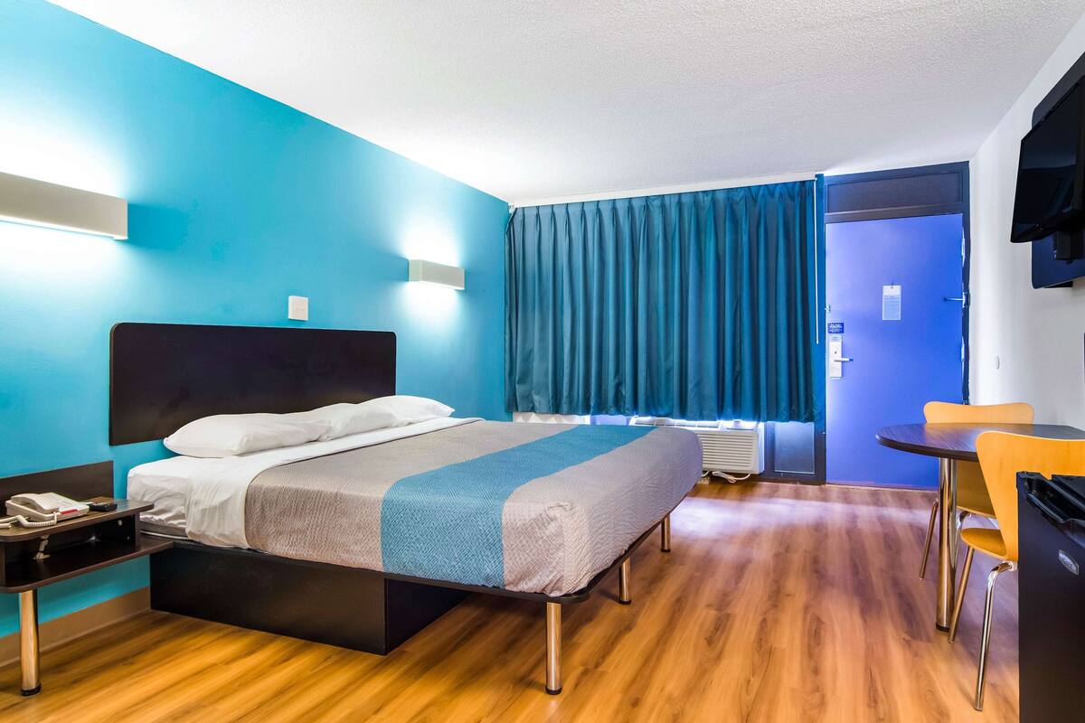A hotel room with a bed, bedside table, and a desk with a chair.