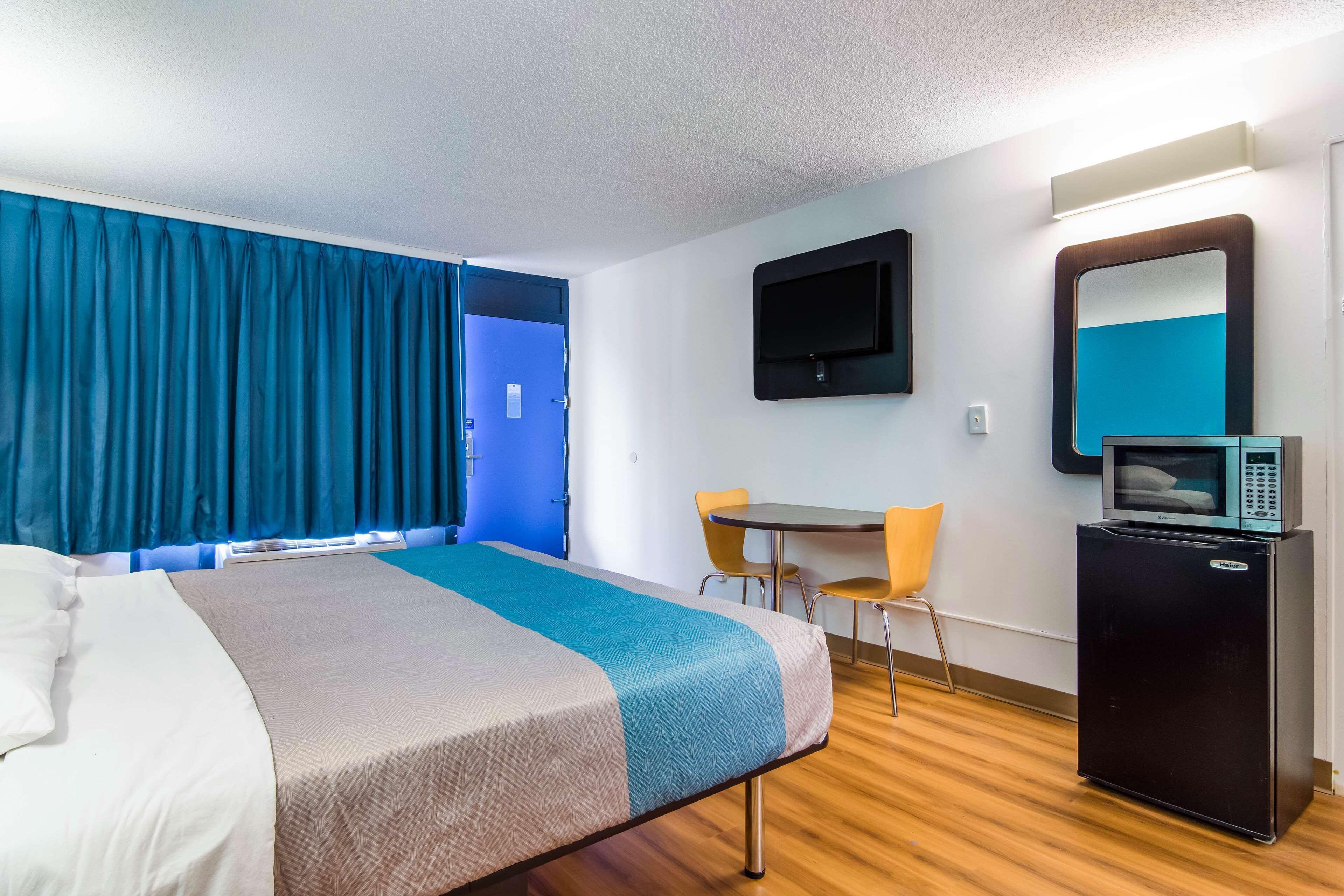 A hotel room with a bed, a desk, a chair, a television, and a refrigerator.