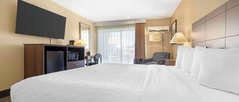 Une chambre d’hôtel avec un grand lit, un téléviseur à écran plat, un bureau avec un ordinateur, une chaise et une fenêtre avec des rideaux.
