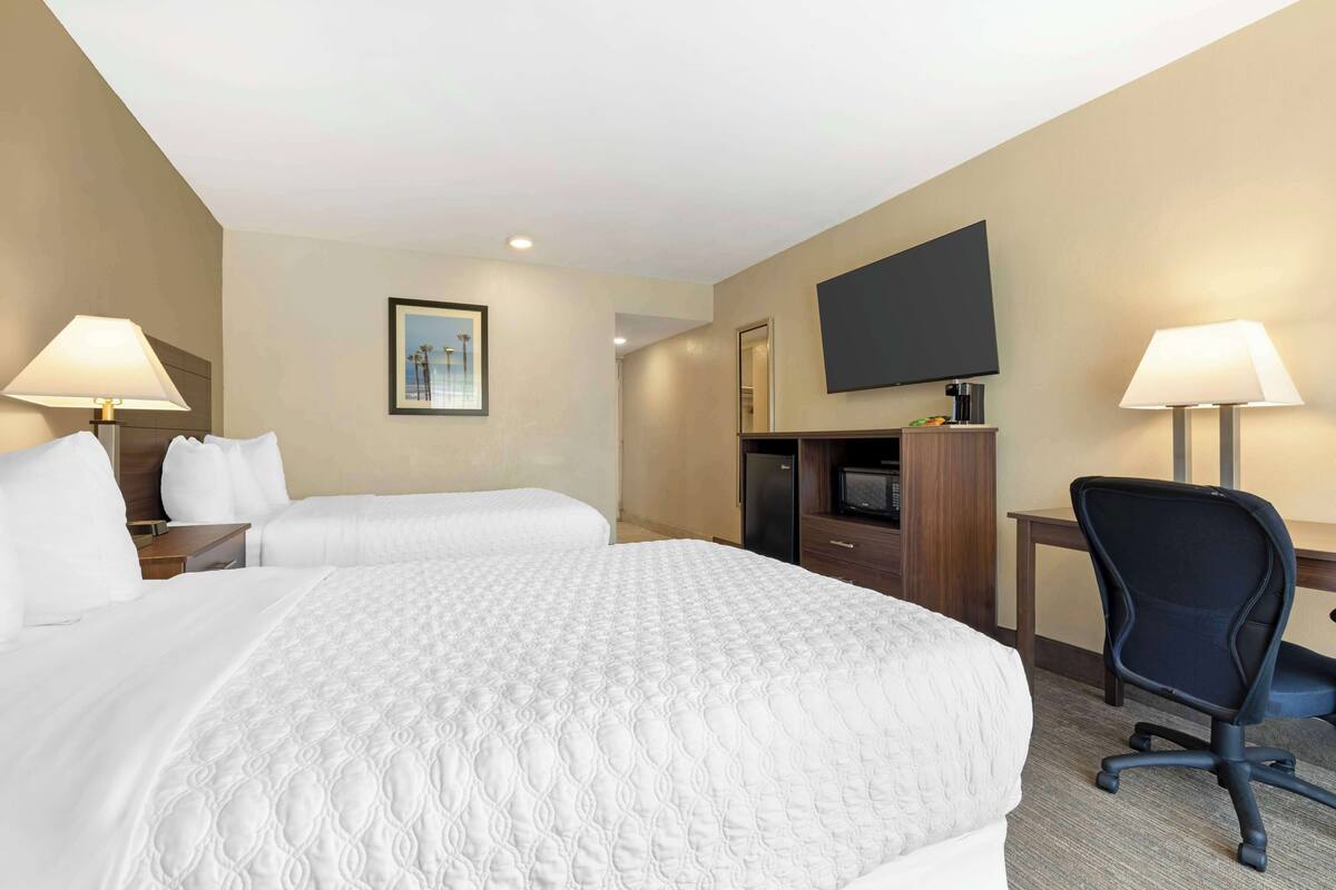 A hotel room with two beds, a desk, a chair, a flat-screen TV, and a framed picture on the wall.