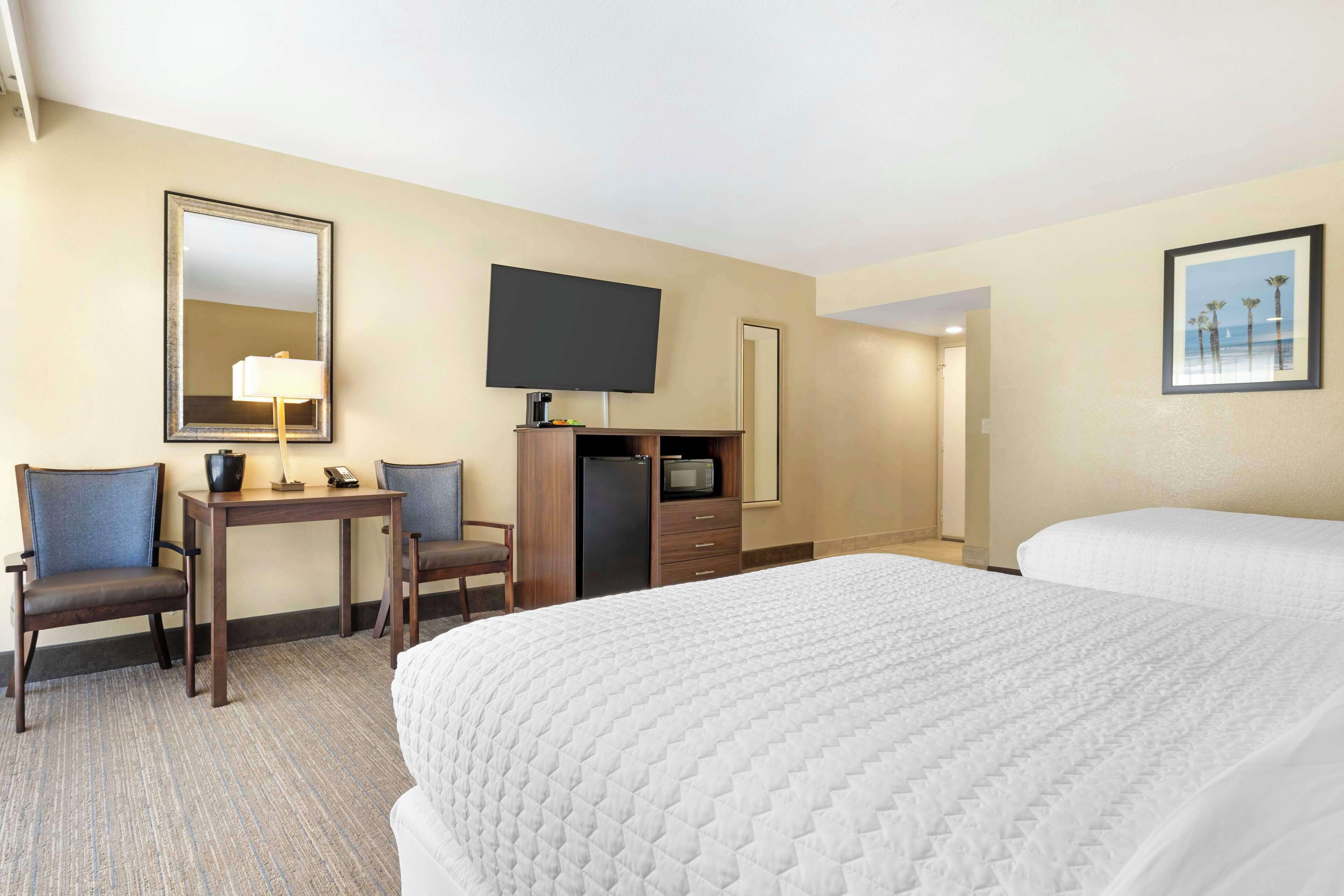 A hotel room with a large bed, a desk with a chair, a television, and a mirror.
