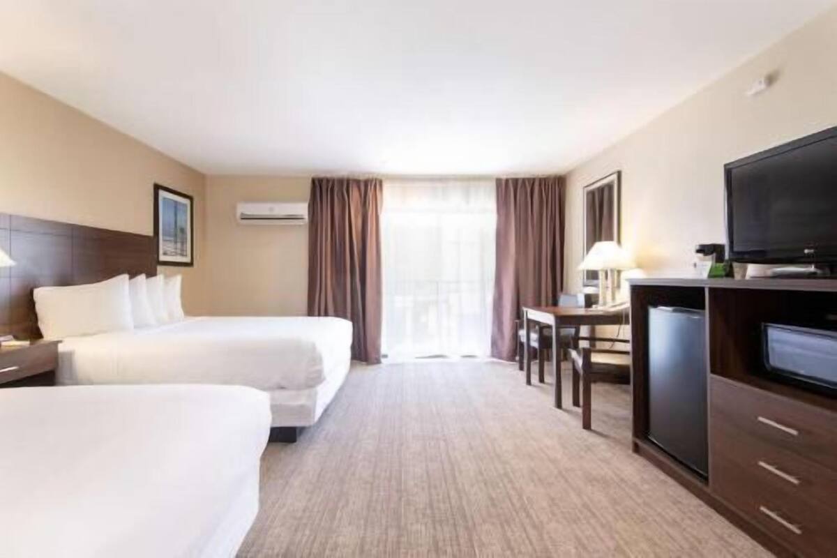 A hotel room with two beds, a desk, a television, and a window with curtains.
