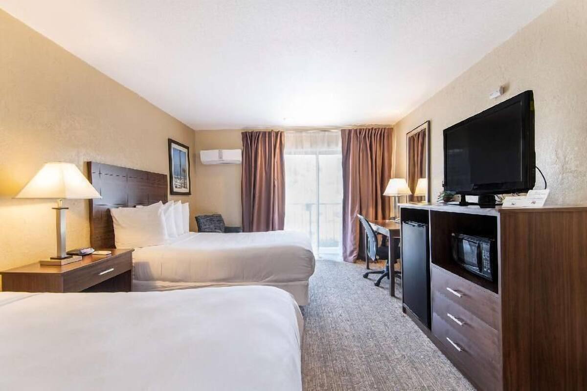 A hotel room with two beds, a desk, a television, and a microwave.