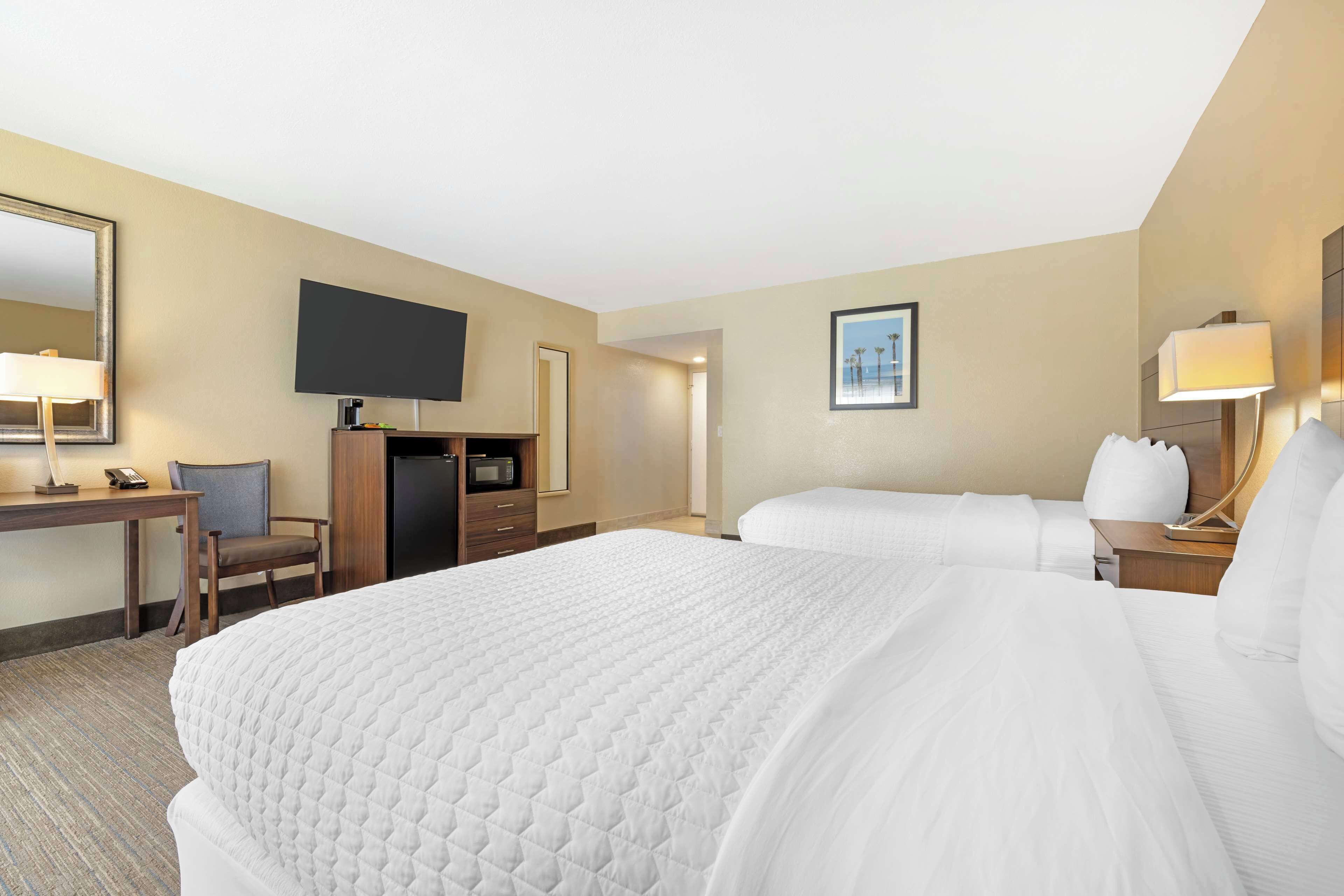 A hotel room with a large bed, a desk with a chair, a television, and a framed picture on the wall.