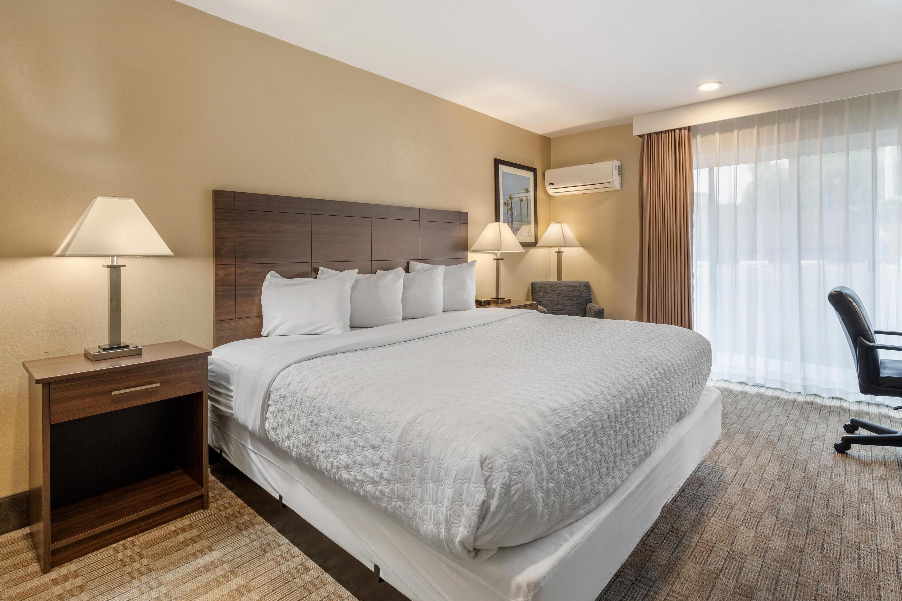 A hotel room with a large bed, two bedside tables with lamps, a chair, and a window with curtains.