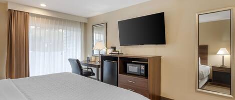 A hotel room with a large bed, a desk with a computer, a microwave, and a flat-screen TV.