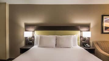 A hotel room with a large bed, two bedside lamps, a telephone, and a patterned chair.