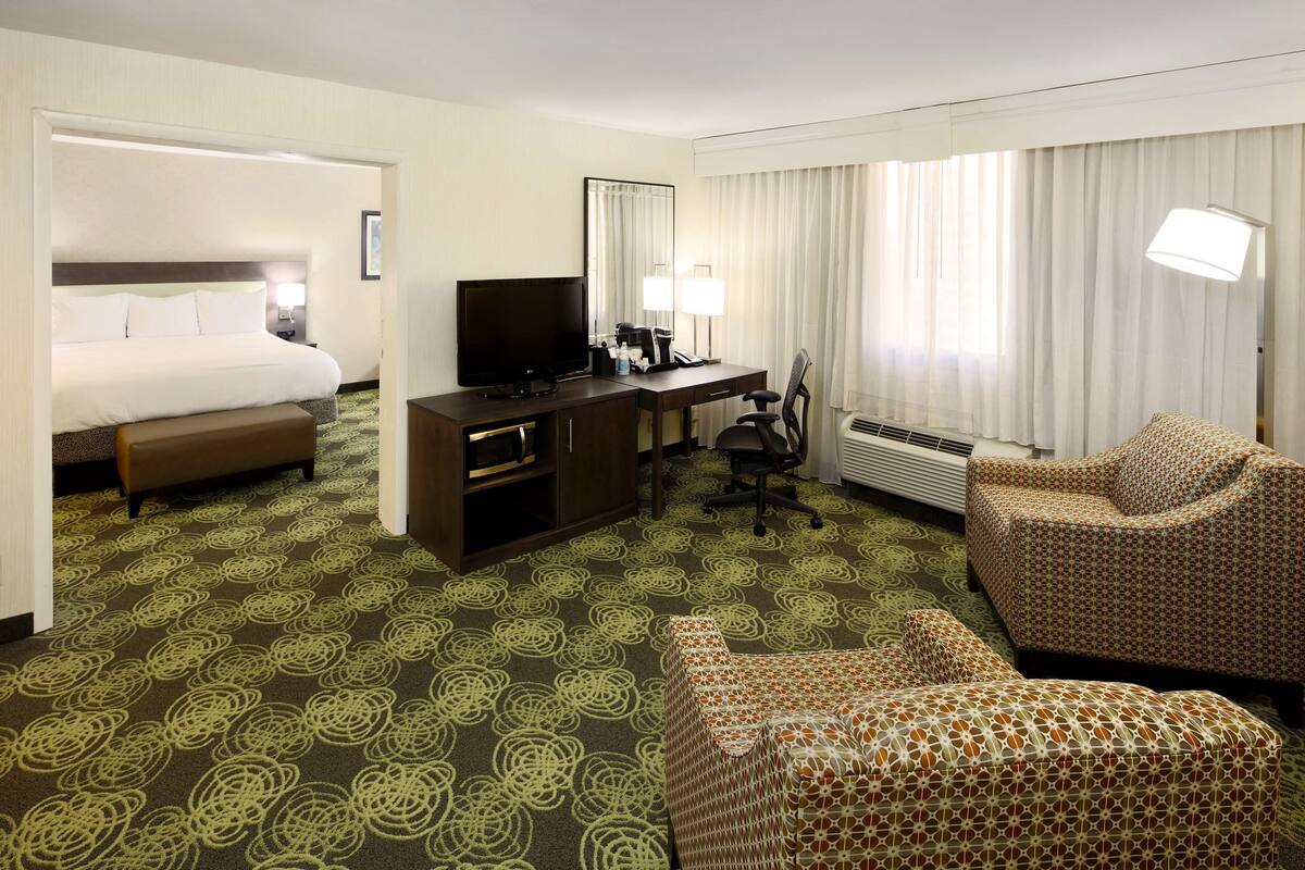 Ein Hotelzimmer mit Bett, Schreibtisch, Fernseher, Sessel und Sofa.