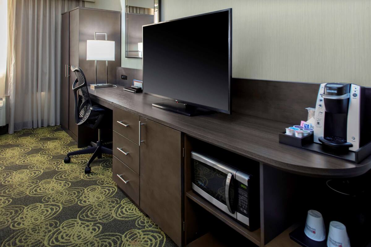 Ein Hotelzimmer mit Flachbildfernseher, Schreibtisch mit Lampe, Mikrowelle und Kaffeemaschine.