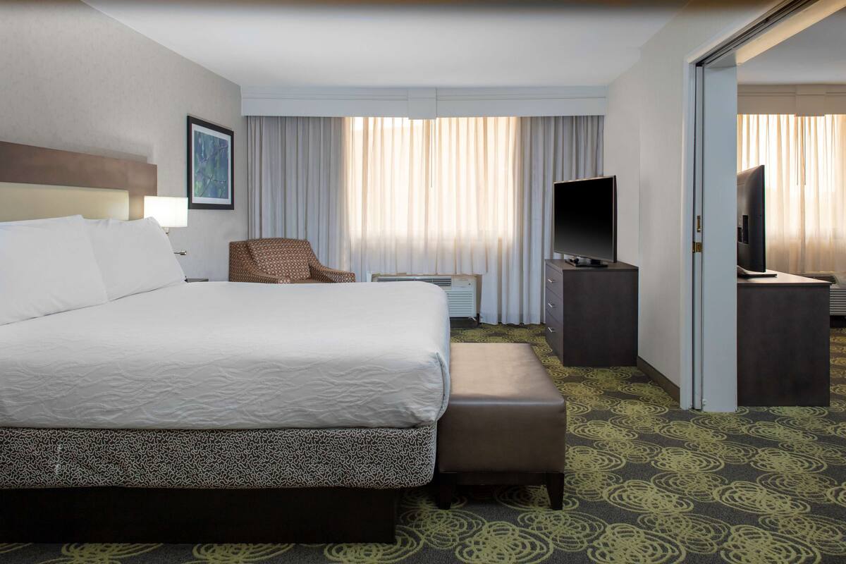 Ein Hotelzimmer mit einem großen Bett, einem Sessel, einem Fernseher und einem Schreibtisch.