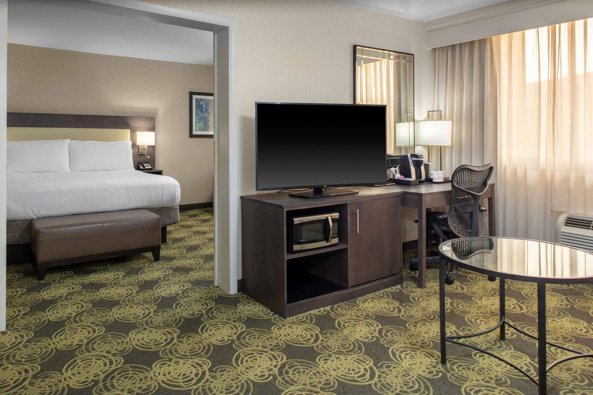 Ein Hotelzimmer mit einem Bett, einem Flachbildfernseher, einem Schreibtisch mit Stuhl, einer Mikrowelle und einem Glastisch.