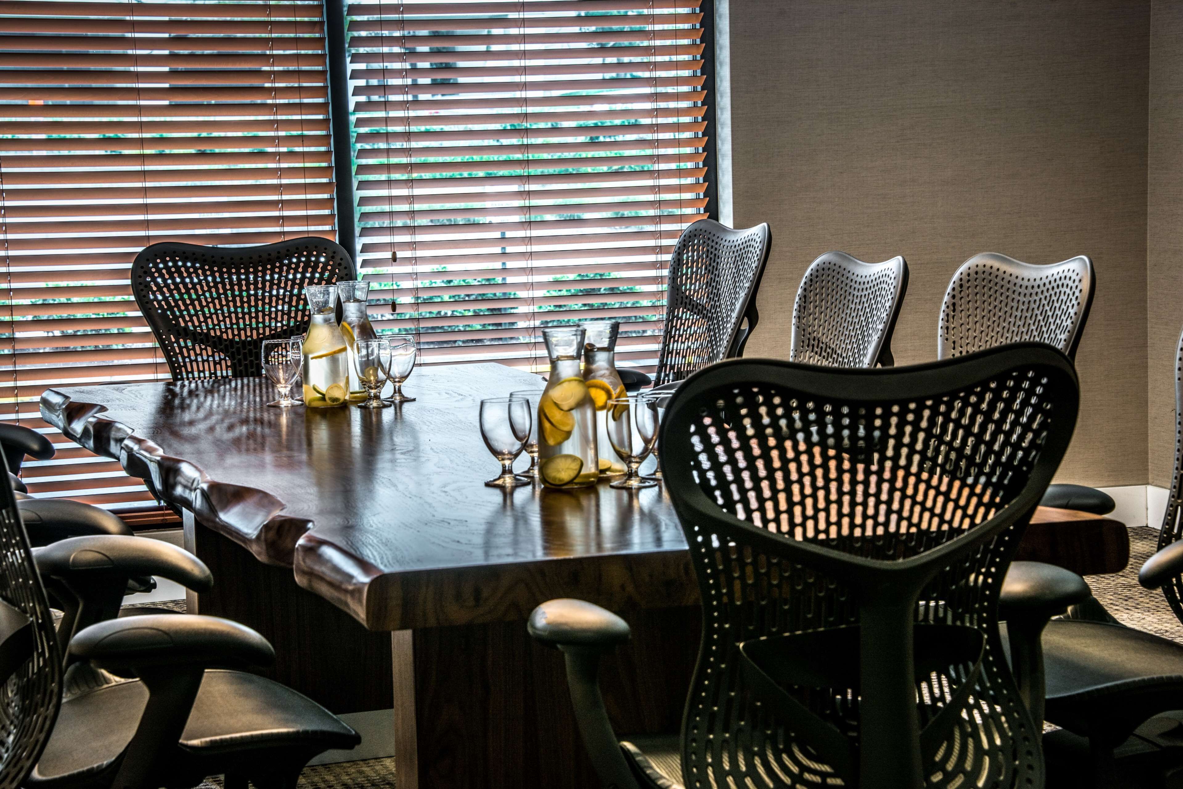 A conference room with a long table, black mesh chairs, and a window with blinds.