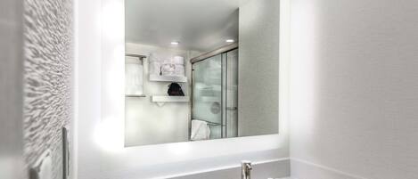 A modern bathroom with a large mirror, a white sink, and toiletries on the counter.
