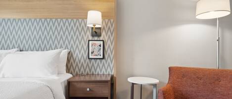 A hotel room with a bed, a nightstand, a lamp, a small table, and a sofa.
