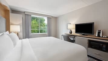 Une chambre d’hôtel avec un grand lit, une télévision, un bureau avec une lampe et une fenêtre avec des rideaux.