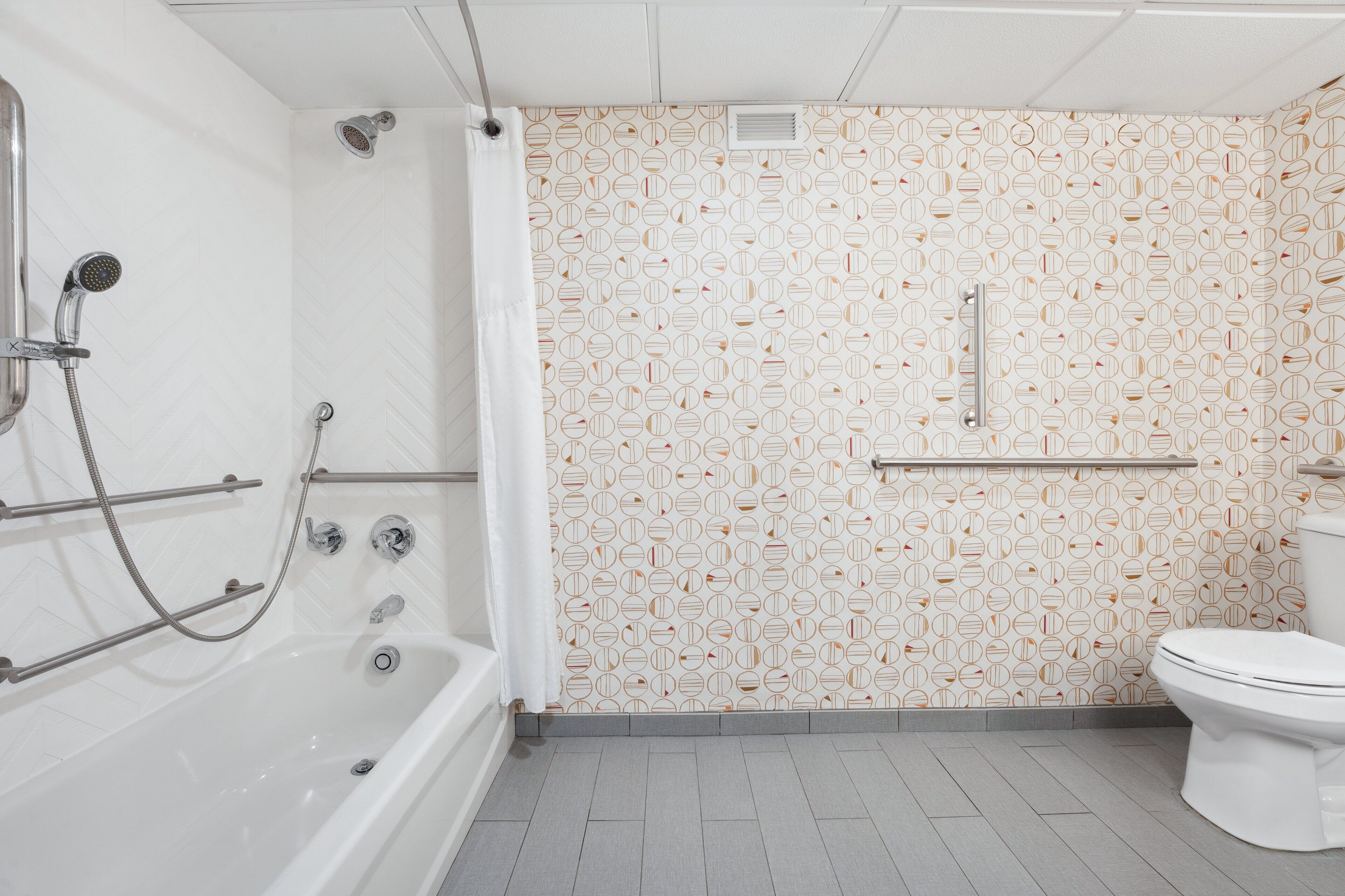 Un baño con bañera, ducha, inodoro y un papel tapiz estampado.