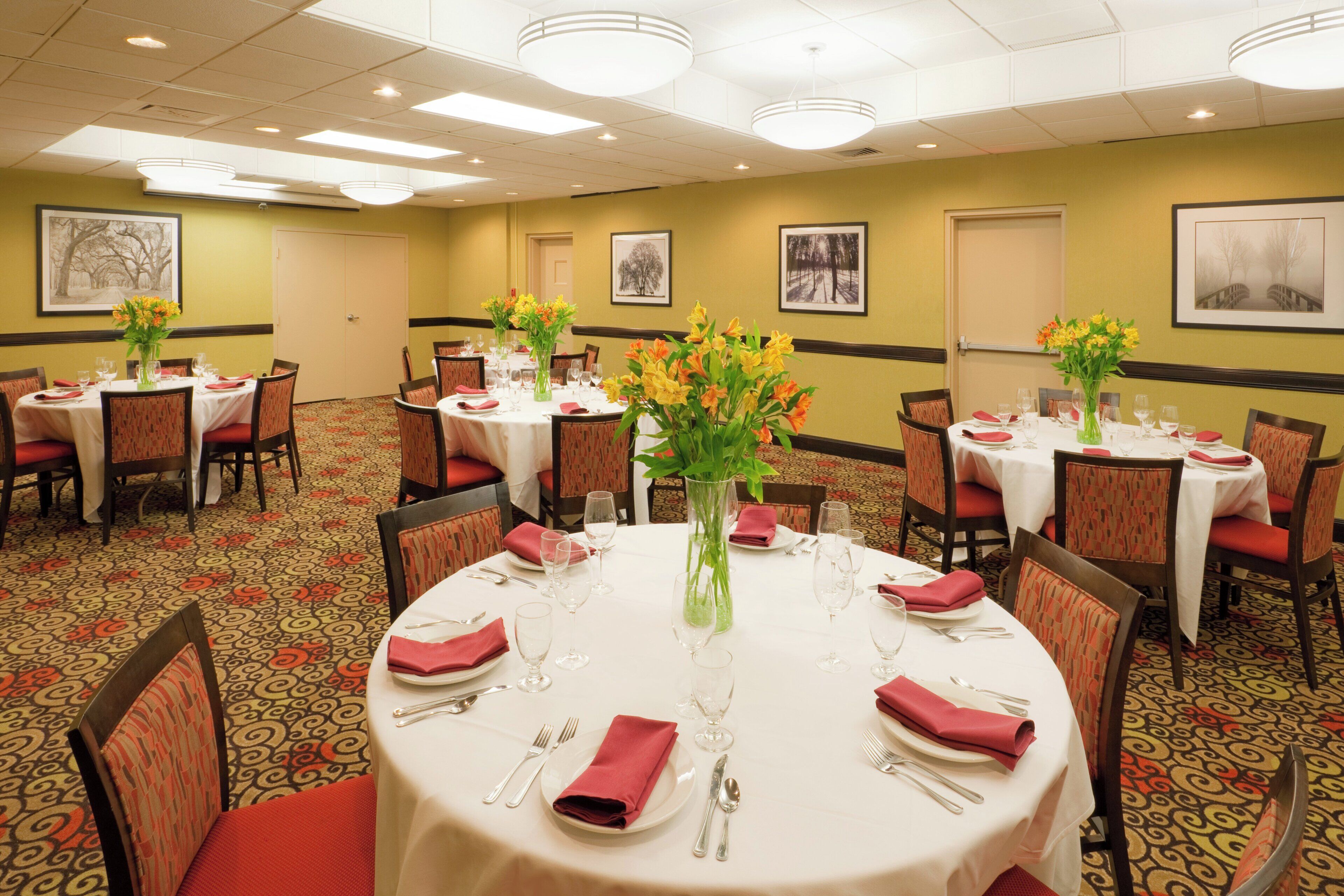 A hotel dining area with round tables, chairs, and floral centerpieces.